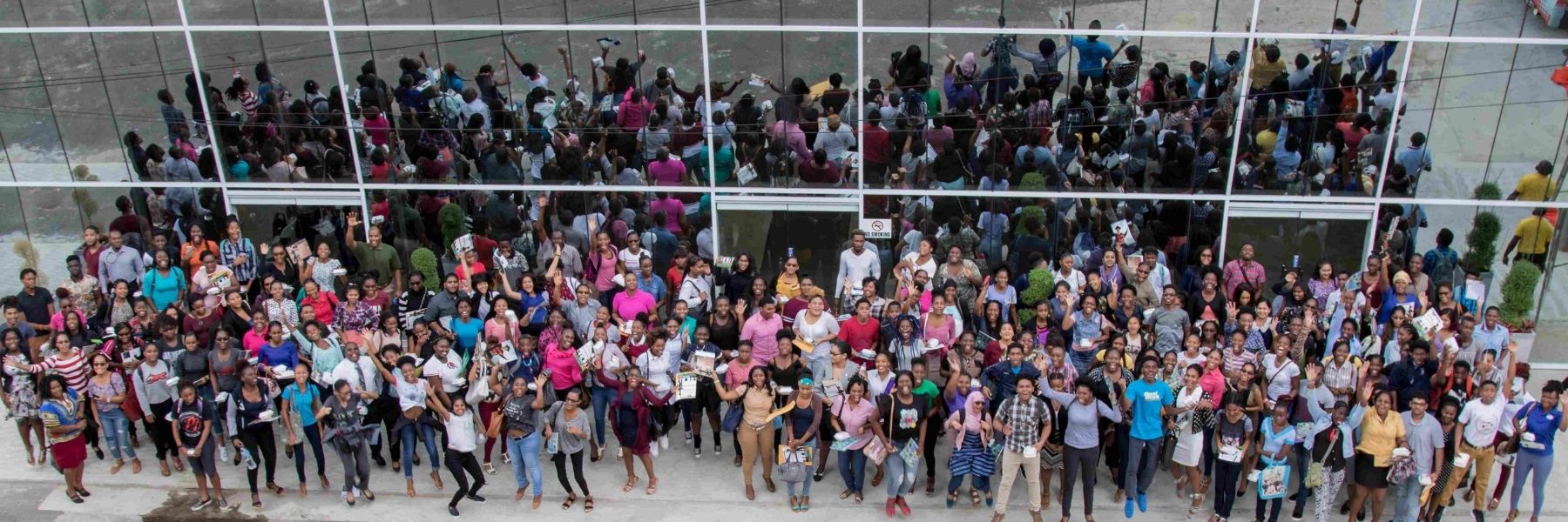 An aerial view of a large, diverse, and enthusiastic crowd of students and visitors gathered in front of a modern campus building, visually answering the question of Why choose USC by showcasing its vibrant and welcoming community.